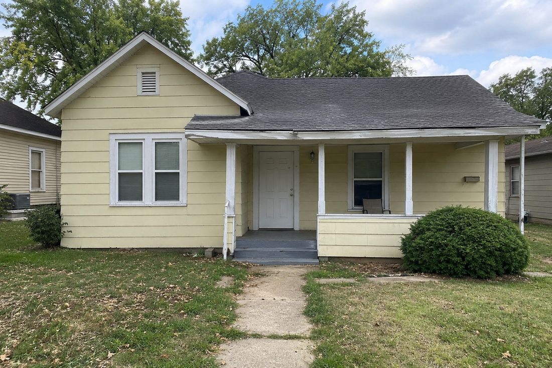 A yellow cottage with a front porch and shrubs